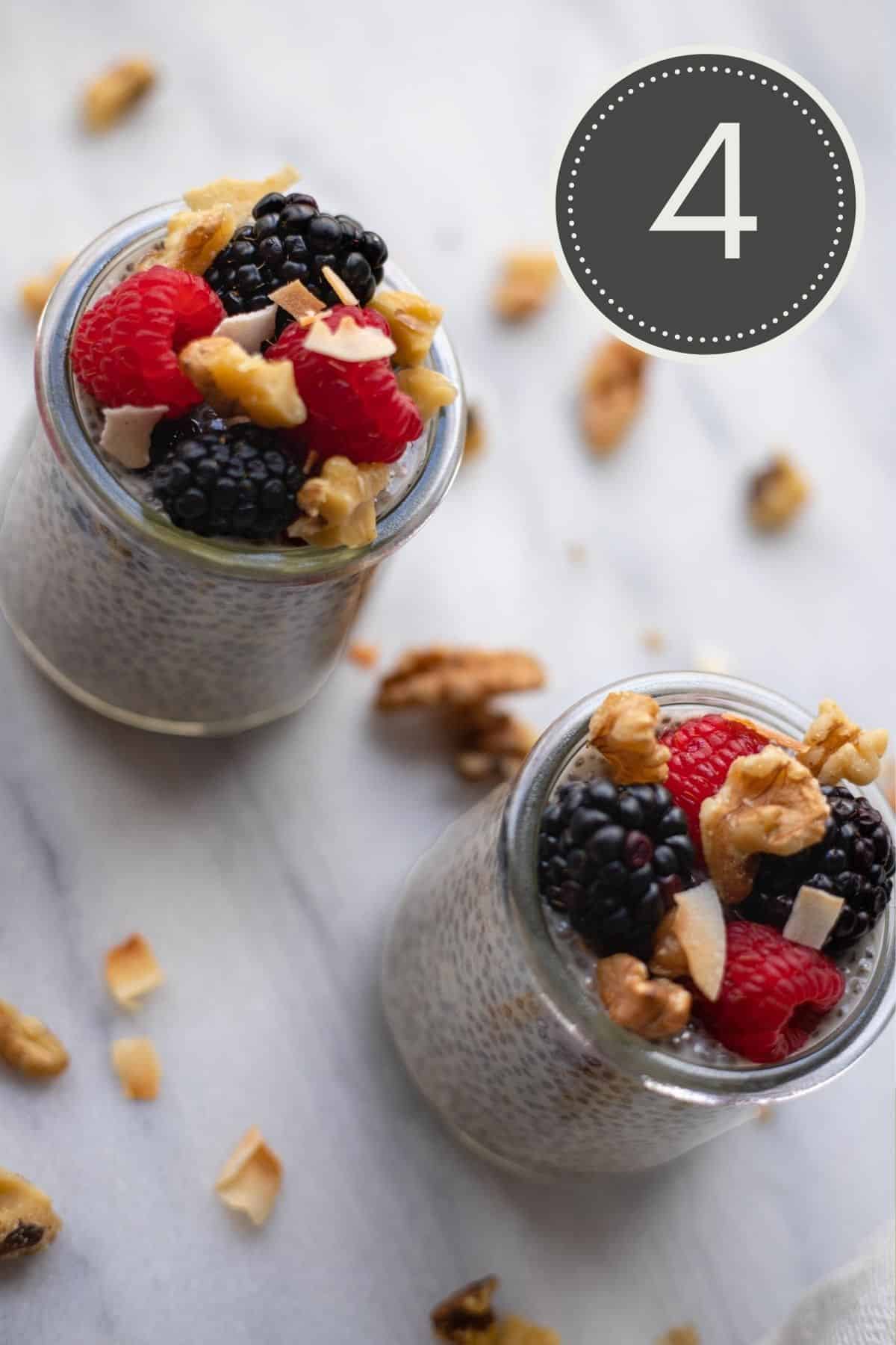 Top down view of two glass jars filled with chia pudding showing berries and nuts used as toppings.