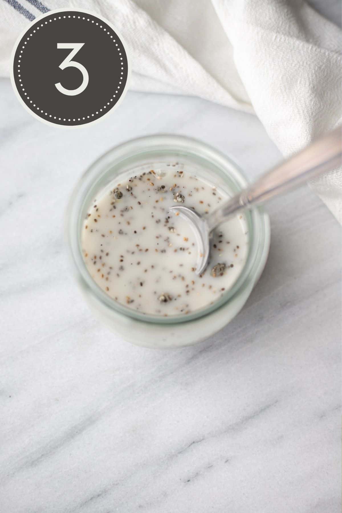 Step three of the recipe showing a spoon mixing the wet and dry ingredients together in the glass jar.