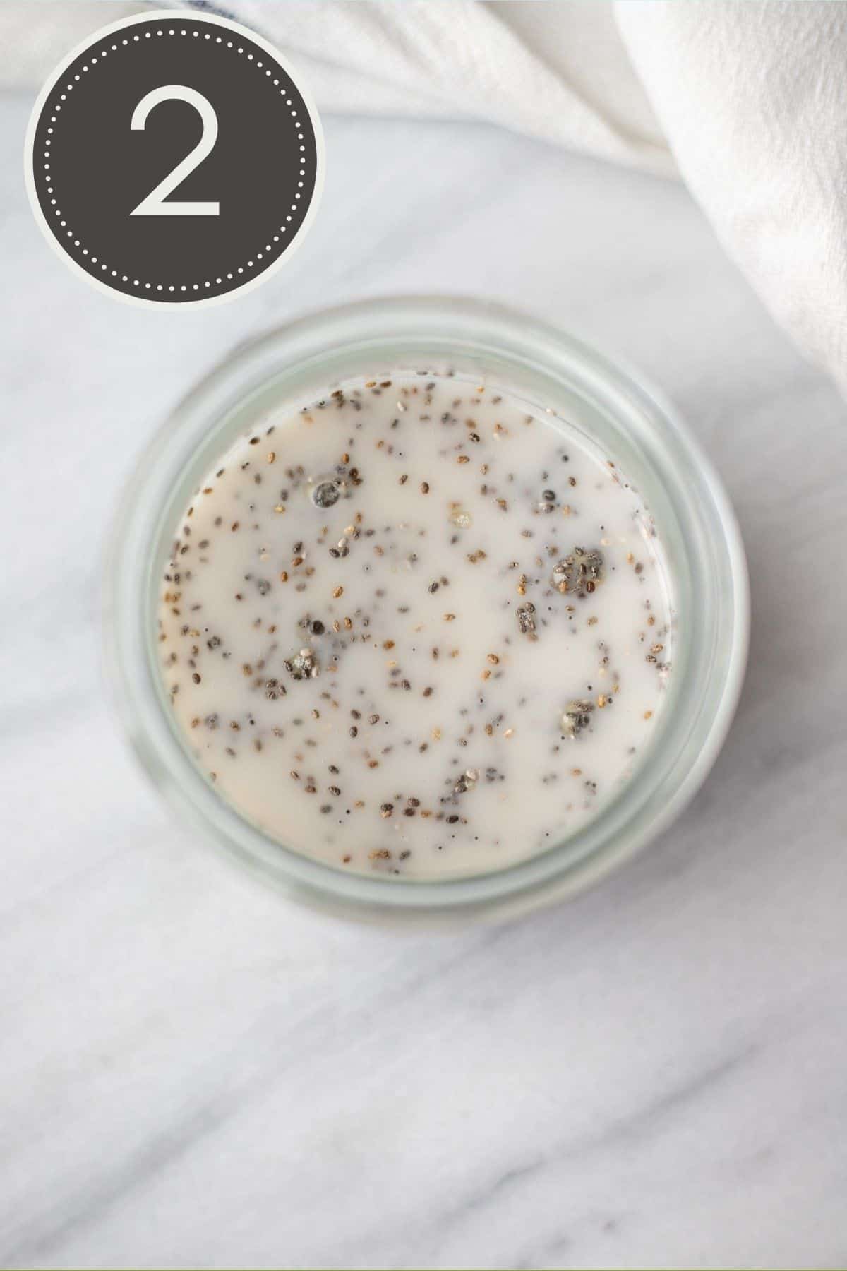 Step two of the recipe showing the wet ingredients of plant-based milk and vanilla mixed in with the dry ingredients in the glass jar.