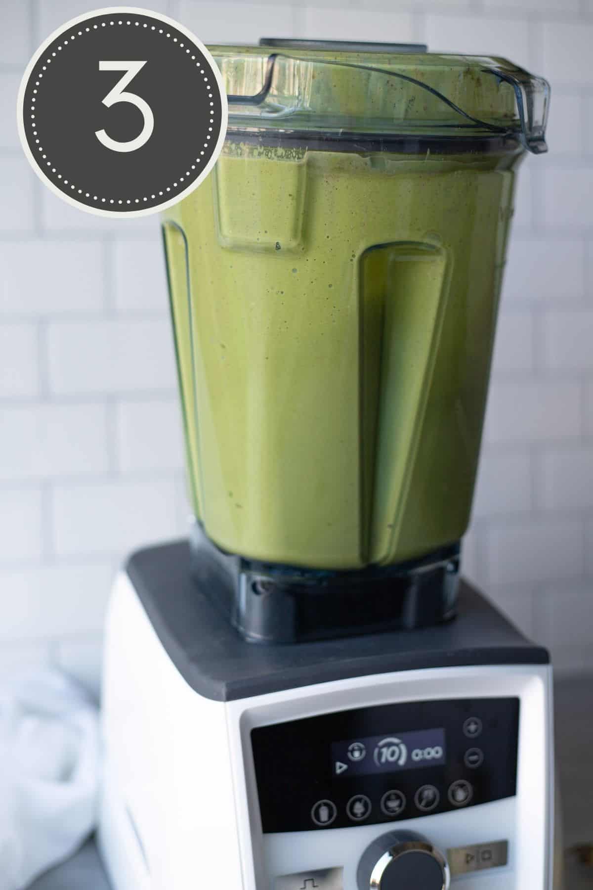A green smoothie in the process of being blended in a blender on a kitchen counter.
