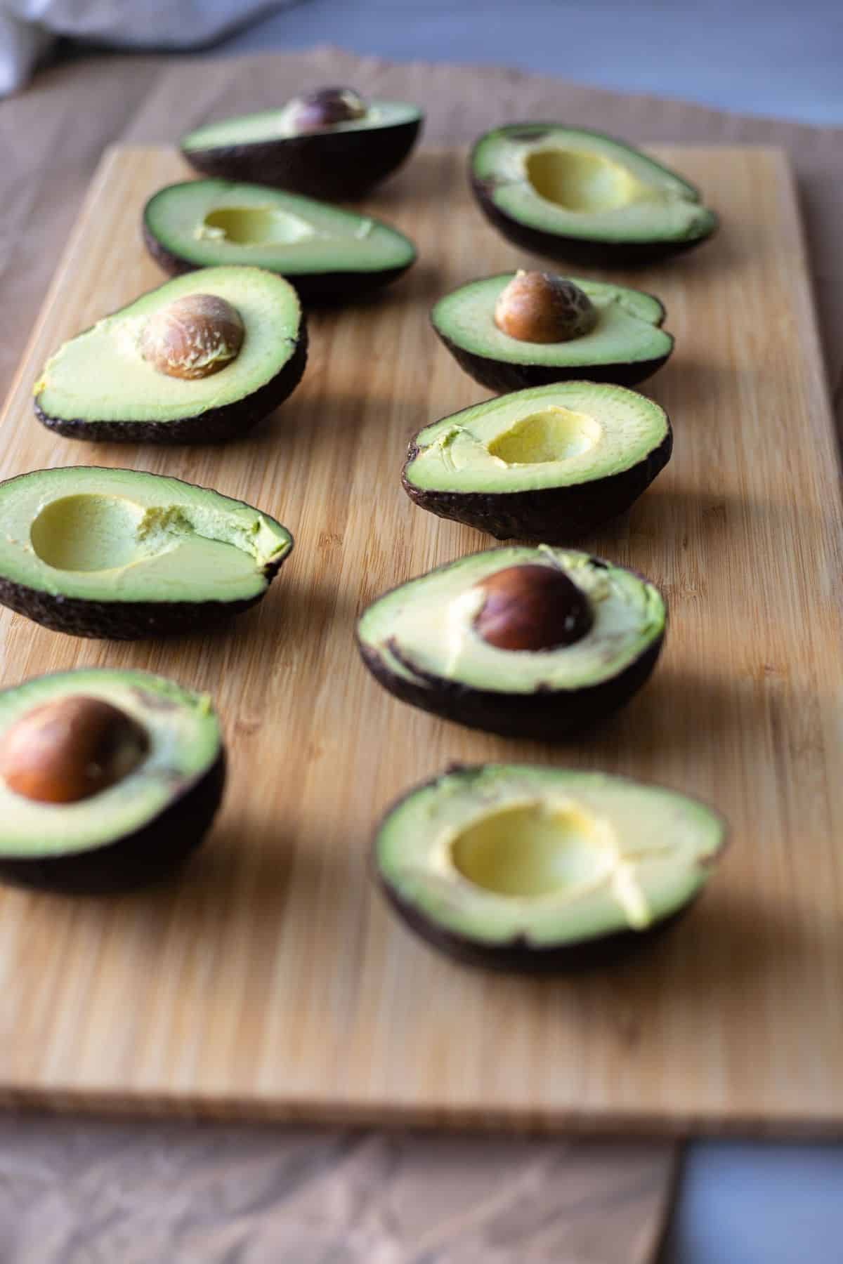 Avocado halves cut facing upward on a wooden cutting board.