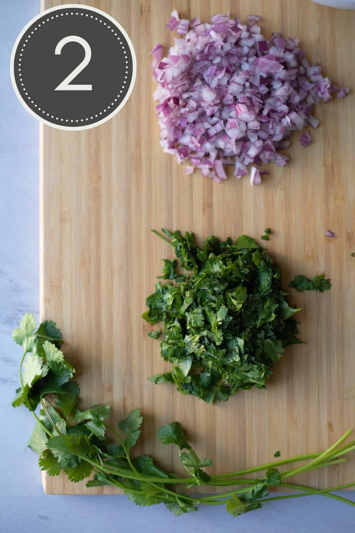 Chopped red onion and chopped cilantro on a wooden cutting board.