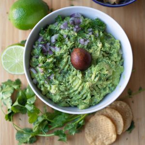 Top down view of guacamole in a bowl with chips, cilantro, and a lime around it.