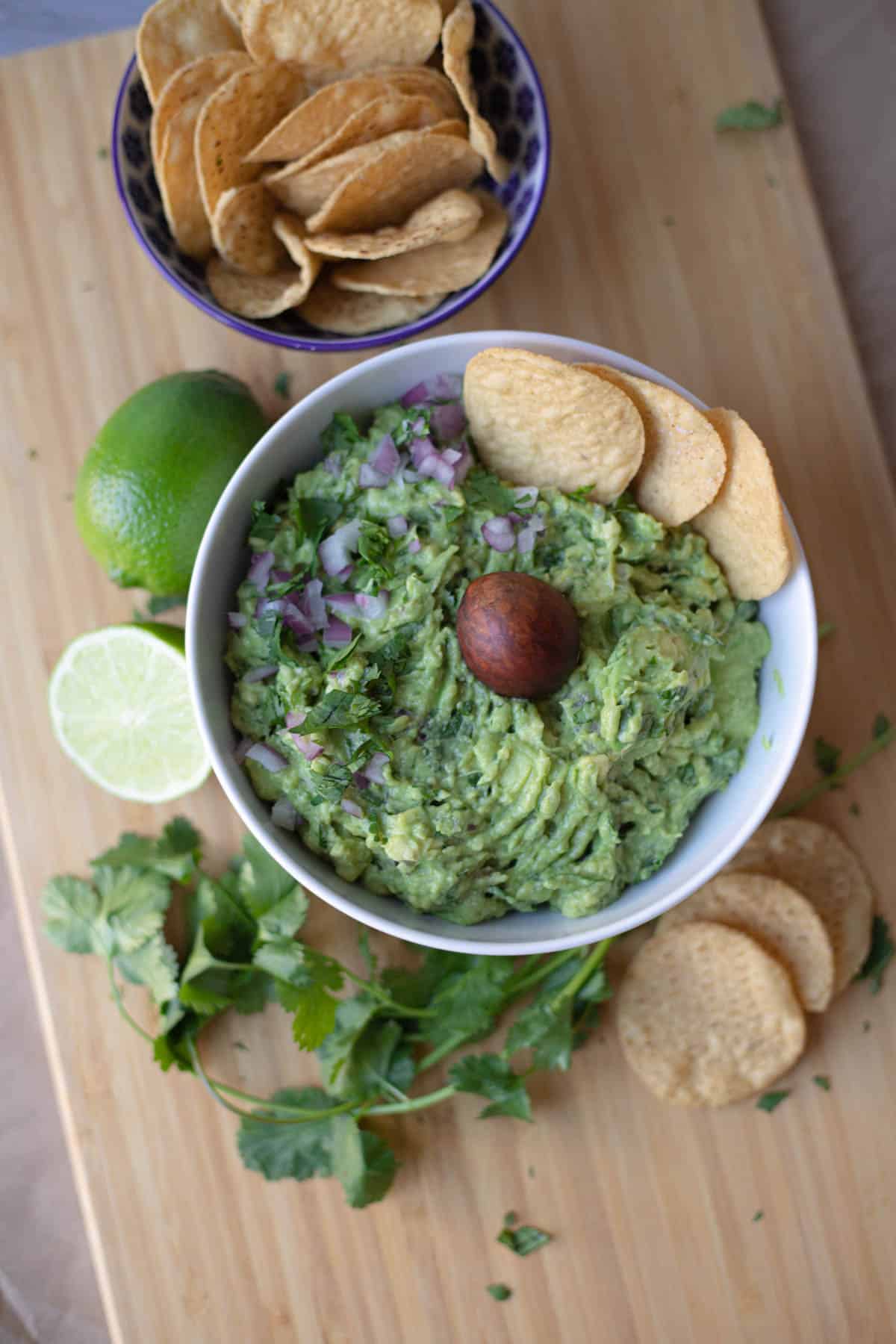 Guacamole in a white bowl with chips in the dip and in a blue bowl to the side of the dip.