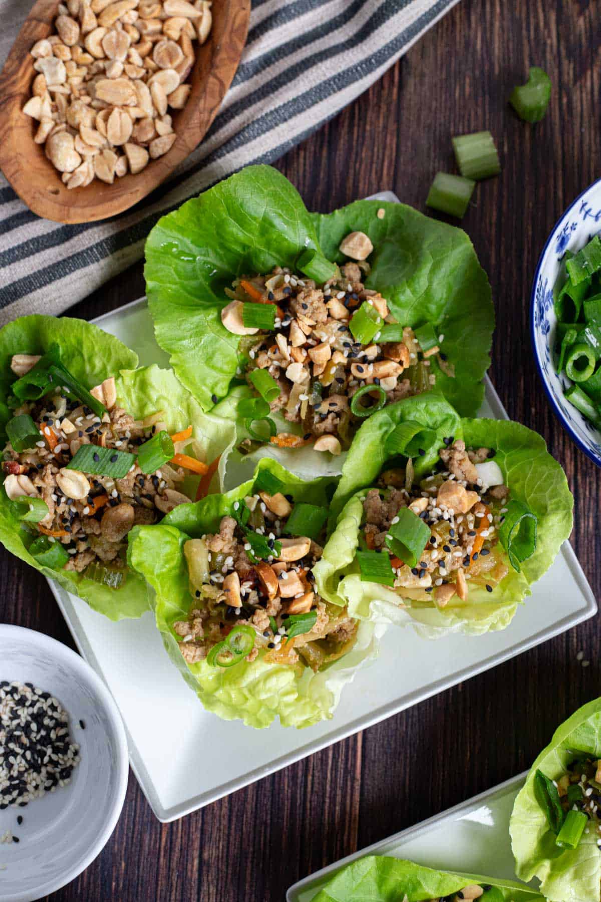 four lettuce cups filled with ground turkey, peanuts, and green onions on a white plate that is sitting on a dark wood table.