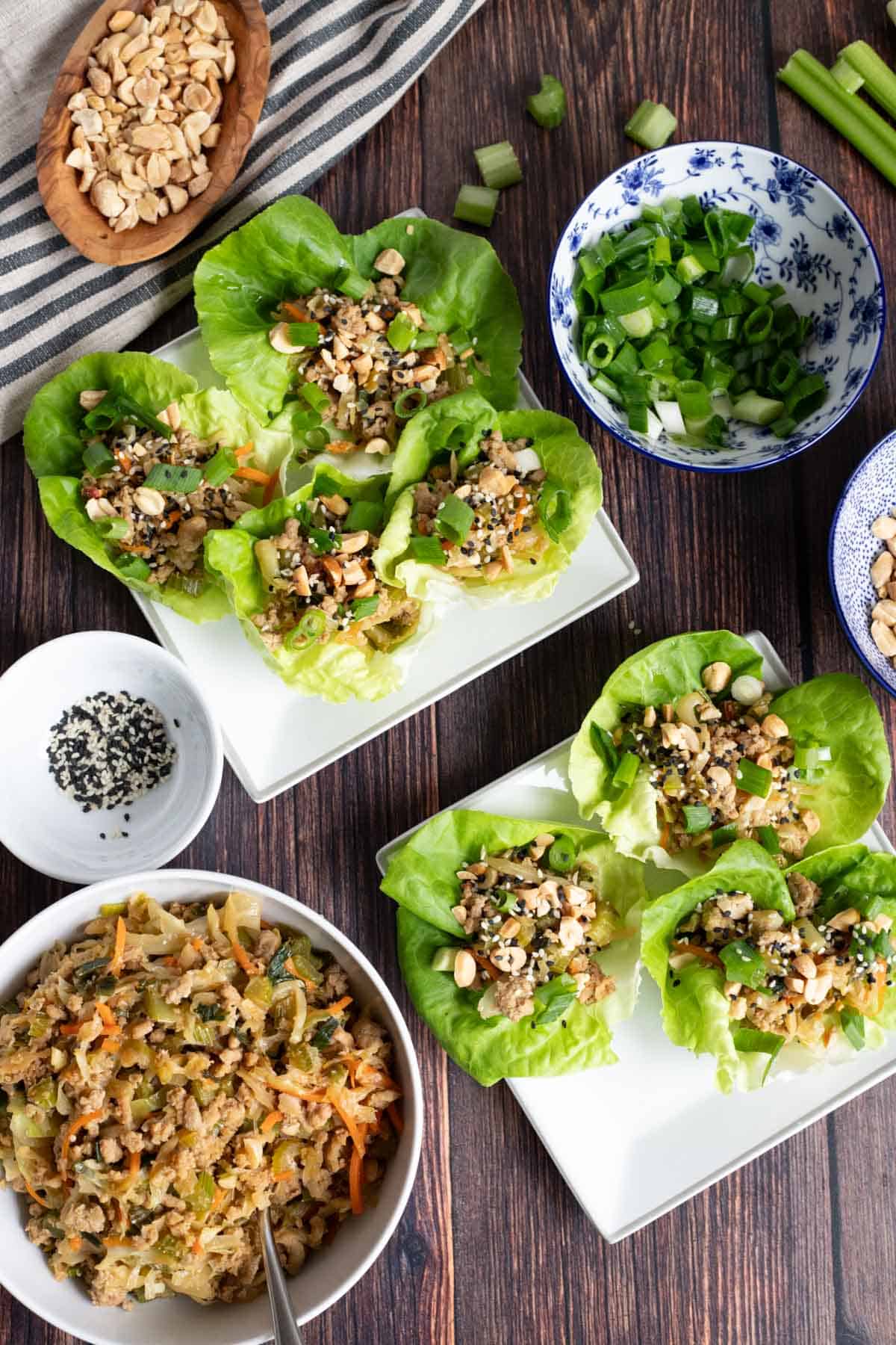 top down, finished view of lettuce wraps filled with ground turkey mixture on plates surrounded by recipe ingredients on a wooden table.