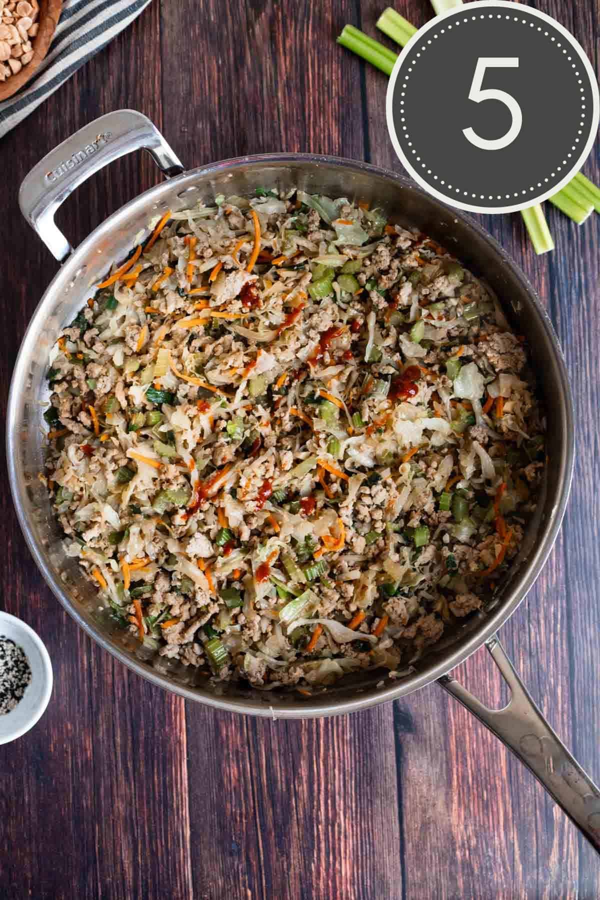 ground turkey mixture cooking in a stainless steel pan with a dash of sriracha on top.