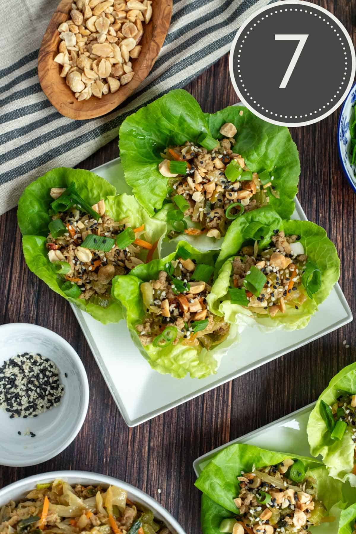 asian lettuce cups filled with ground turkey, topped with peanuts, green onions, and sesame seeds, plated on a wooden table.
